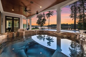 A hot tub with a view of a sunset over a lake, surrounded by trees and a wooden ceiling.