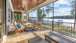 En rymlig, inglasad veranda med trägolv, en takfläkt och stora fönster som ger utsikt över en sjö och träd.
