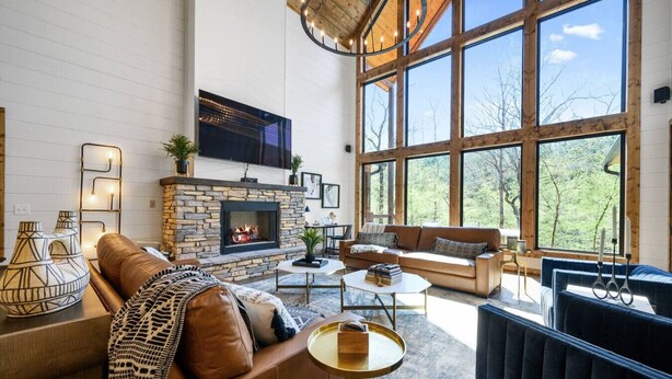 A spacious living room with a stone fireplace, leather sofas, and large windows offering a view of the outdoors.