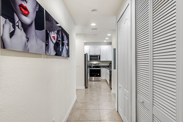 A hallway with a kitchen area, white cabinets, and a tiled floor. - Modern Oasis pool paradise (Cape Coral)