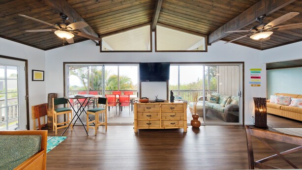 Um quarto amplo com piso de madeira, uma mesa de jantar de madeira com cadeiras, um sofá e um ventilador de teto.