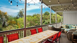 Uma área externa coberta com mesa, cadeiras, luzes de corda e vista para o verde.