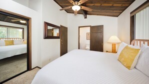 Quarto com cama grande, ventilador de teto, mesa de cabeceira com abajur e porta para outro cômodo.