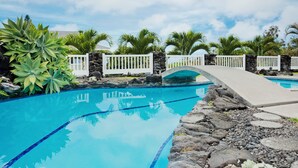 Piscina com borda de pedra, cerca branca e uma ponte.