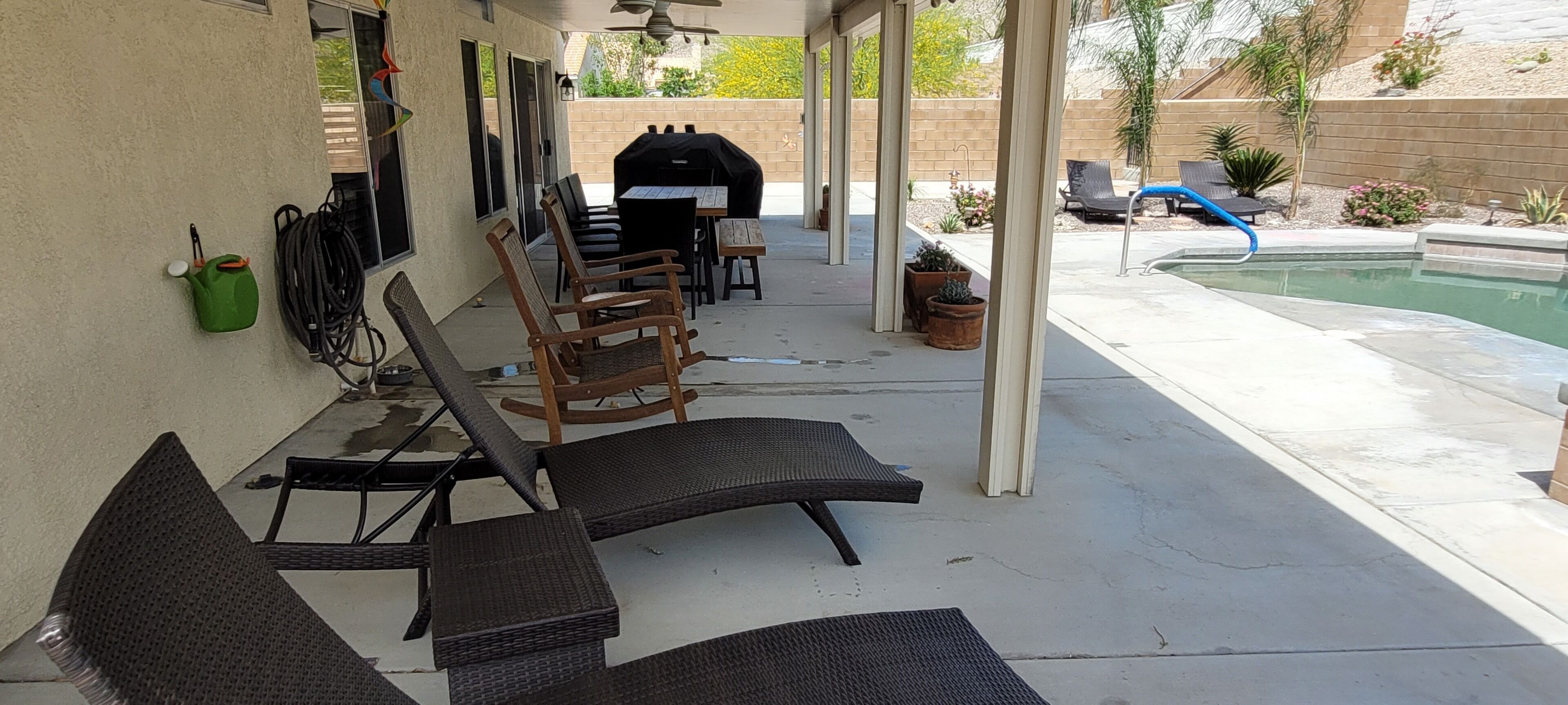 A covered patio with outdoor furniture, a grill, and a pool.