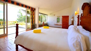 A large bed with white linens and two yellow pillows, a wooden headboard, and a view of a balcony with a railing. - 530674 Vista Mar - Font de Sa Cala - 530674 Vista Mar - Font de sa Cala (Font de Sa Cala)