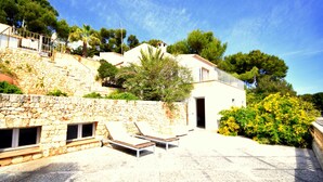 A stone building with a balcony, a stone wall, and a garden with yellow flowers. - 530674 Vista Mar - Font de Sa Cala - 530674 Vista Mar - Font de sa Cala (Font de Sa Cala)