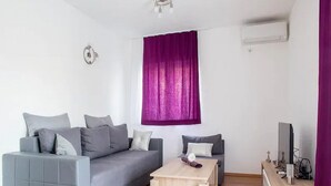 A modern living room with a grey sofa, a wooden coffee table, and a small side table with a speaker. - Holiday Home J&D 2 (Podstrana)