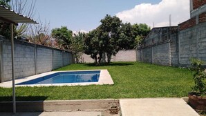 A backyard with a swimming pool, a grassy lawn, and a brick wall. - Aquetzali kin Private House with Pool (Cuautla)