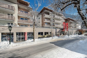 Un edificio a più piani con balconi, una strada in primo piano e neve a terra.