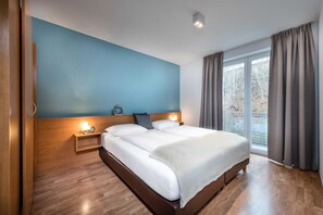A modern hotel room with a large bed, bedside tables with lamps, a wooden headboard, and a view of the outdoors.