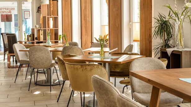 Un restaurant moderne avec des tables et des chaises en bois, de grandes fenêtres et un téléviseur à écran plat fixé au mur.