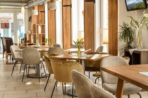 Un restaurante moderno con mesas y sillas de madera, ventanas amplias y un televisor de pantalla plana en la pared.