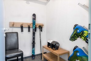 Una sala de esquí con una silla, un soporte de madera con esquíes, una mesa con cascos y un bastón de esquí.