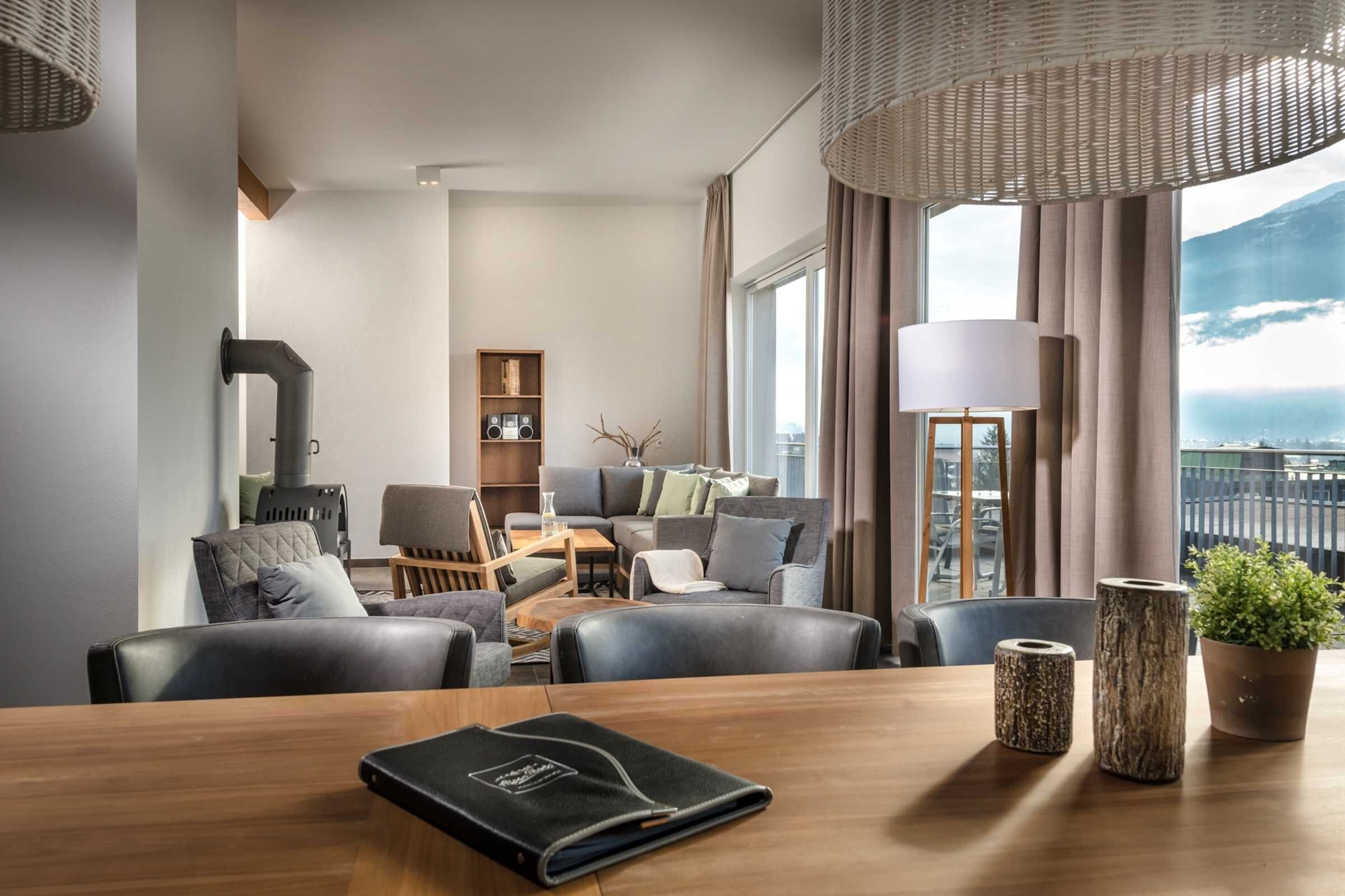 Una habitación de hotel moderna con un conjunto de sofás, una mesa de comedor, una estantería y vistas a la montaña.