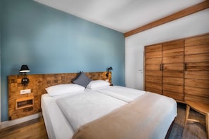 A bedroom with a wooden headboard, a bed with white bedding, a nightstand with a lamp, and a wardrobe.