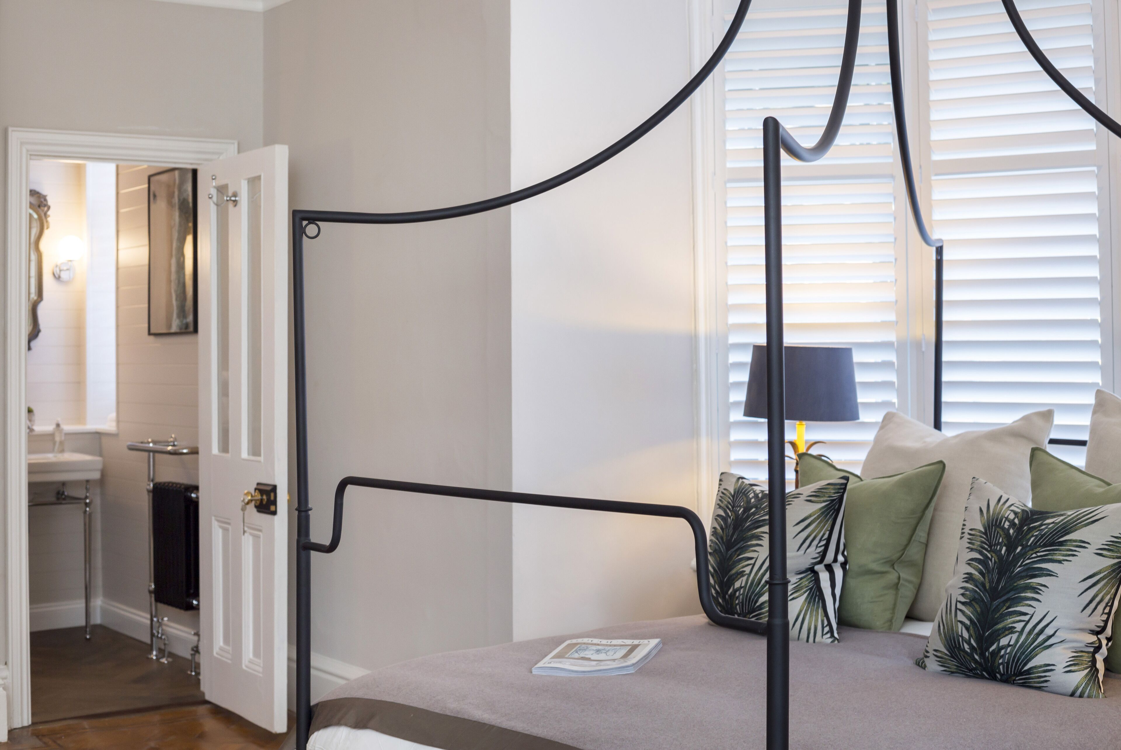 Une chambre à coucher avec un lit à baldaquin, une table de chevet, une lampe et une fenêtre avec des stores.