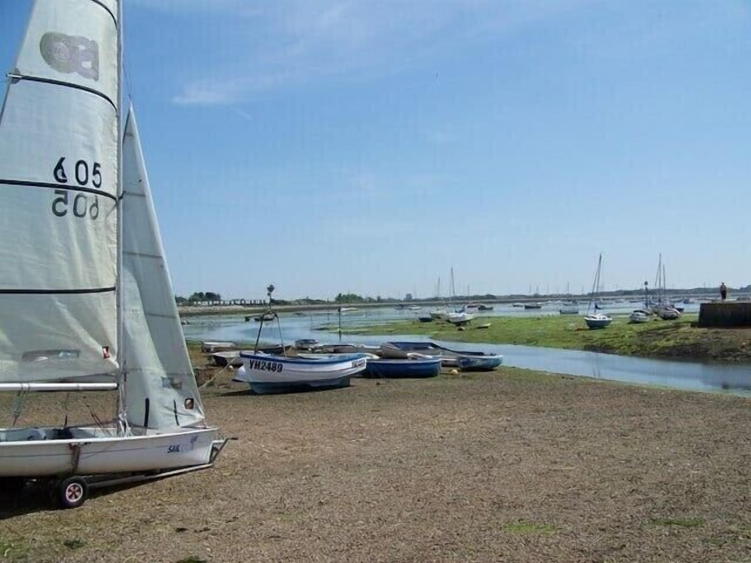 A sailboat with the number 605 docked near a calm river with several other boats.