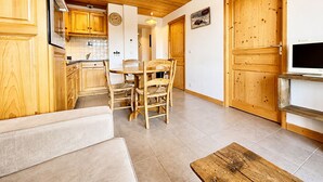 A cozy room with wooden walls and ceiling, a dining area with a table and chairs, a sofa, and a TV on a wooden stand. - Charming apartment with Mont Charvin view and parking (Notre-Dame-de-Bellecombe)