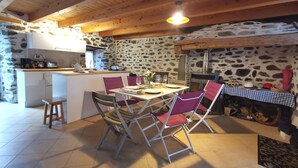 Une cuisine rustique avec des murs en pierre, des poutres en bois, un coin repas avec des chaises et un petit îlot central équipé d’appareils de cuisine.