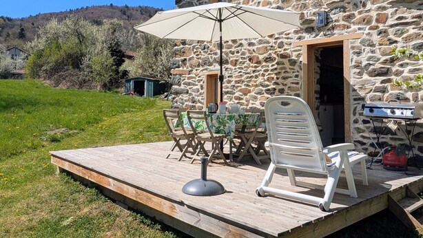 Un bâtiment en pierre doté d’une terrasse en bois, d’une table et de chaises d’extérieur, ainsi que d’un barbecue.