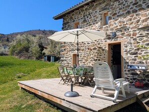 Ein Steinhaus mit einer Holzterrasse, einem Tisch, Stühlen und einem Grill im Freien.