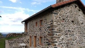 Une maison en pierre avec une cheminée, un petit patio et une vue sur le paysage.
