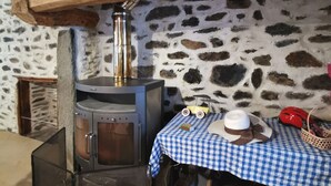 Un mur de pierres, une poutre en bois, un poêle, une table recouverte d’une nappe à carreaux et un chapeau.