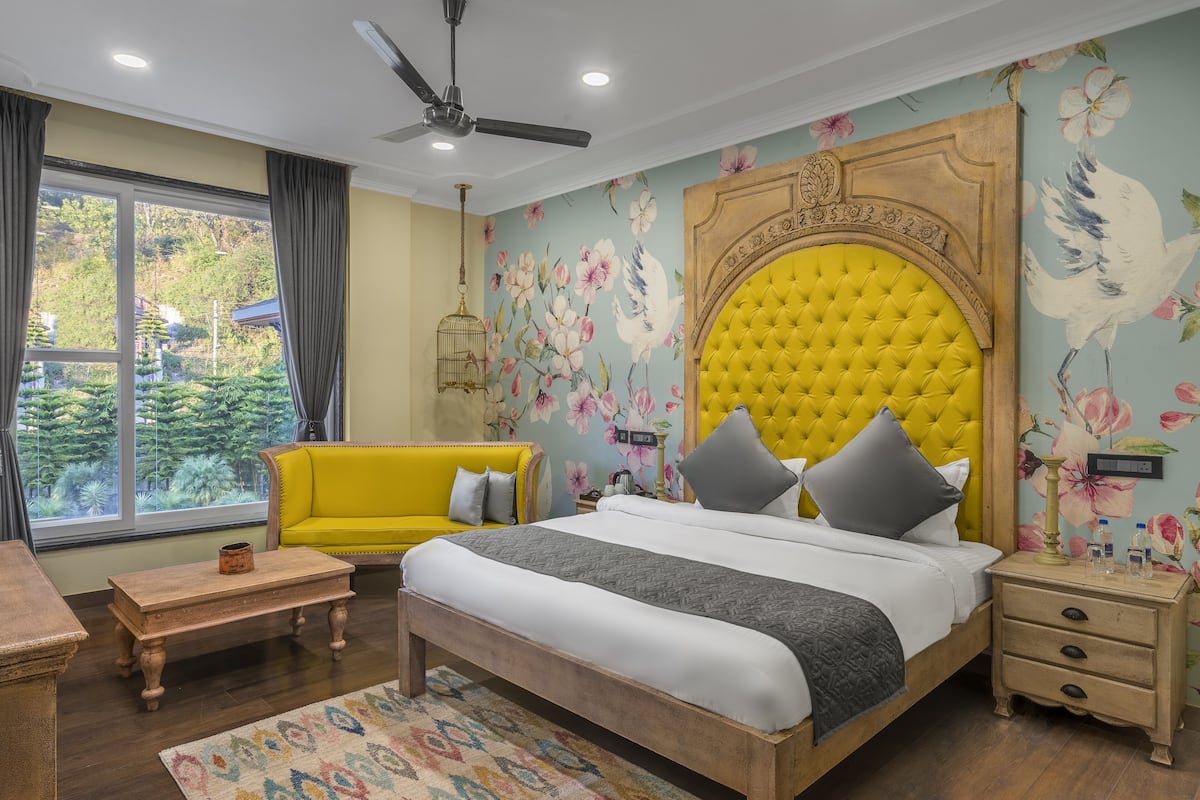 A bedroom with a large bed, a yellow sofa, a wooden nightstand, and a window with curtains.