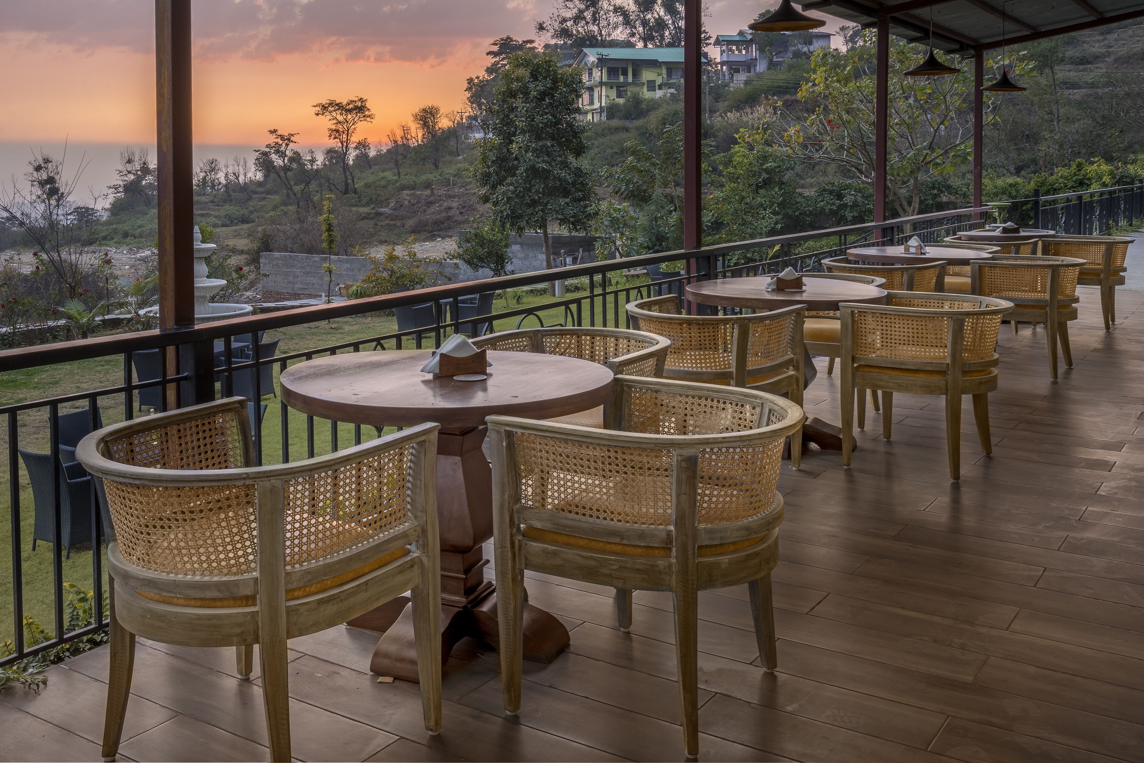 A terrace with wicker chairs and tables, overlooking a scenic landscape with hills and a body of water during sunset.