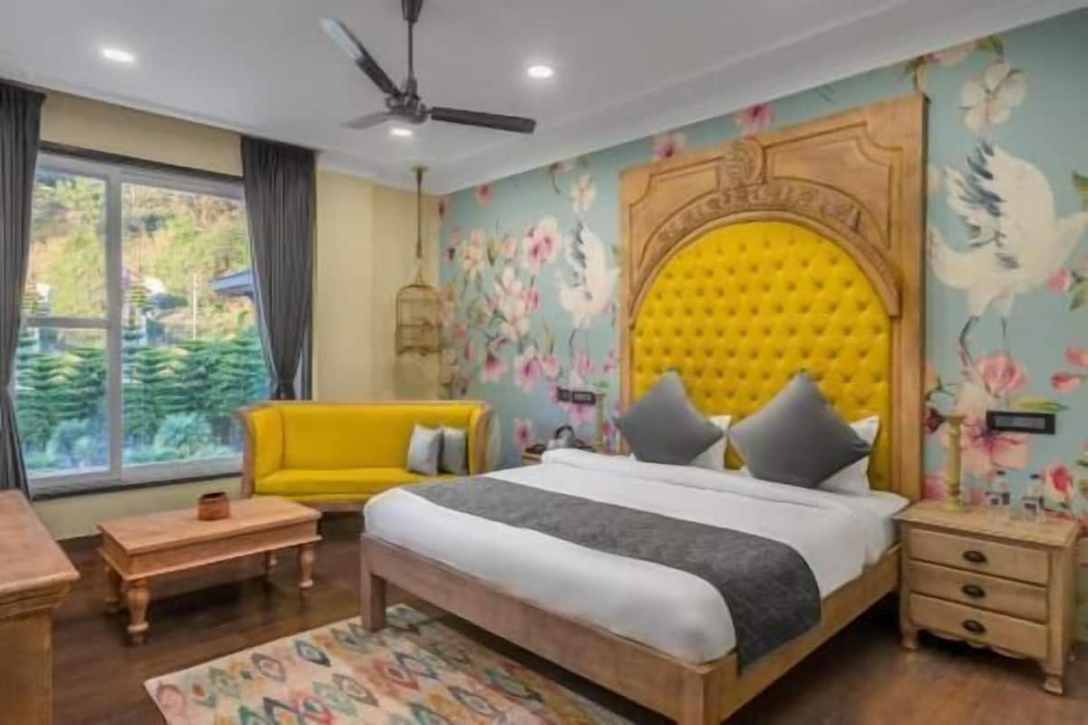 A bedroom with a bed, a yellow sofa, a wooden nightstand, and a ceiling fan.