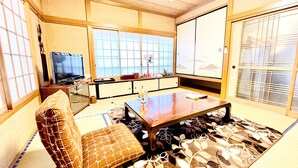 Ein traditioneller japanischer Wohnraum mit Tatami-Böden, einem niedrigen Holztisch, einer Couch und Schiebetüren.