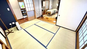 Ein Raum mit Tatami-Matten, einem Futon, einem kleinen Tisch und einem Regal mit Gegenständen.