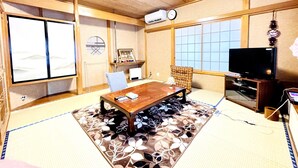 Ein traditioneller japanischer Raum mit Tatami-Böden, einem niedrigen Holztisch, einem Fernseher und einem großen Fenster mit Shoji-Schirmwänden.
