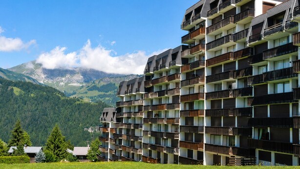 Et hotel med flere etager og balkoner, med et bjergrigt landskab i baggrunden.