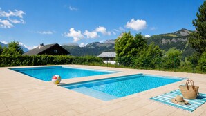 En pool med et bjerg i baggrunden, et hus og et picnicområde.
