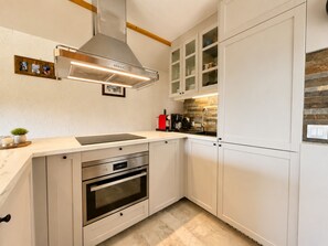 A modern kitchen with white cabinetry, a stainless steel range hood, a built-in oven, and a coffee maker.