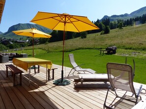 A wooden deck with outdoor furniture, including a table and chairs, and two yellow umbrellas providing shade.