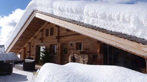 Un chalet en bois doté d’un toit en pente recouvert de neige, de murs extérieurs en bois et d’un petit espace porche.