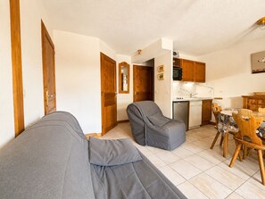 En stue med sofa og skammel, et spisebord med stole, samt et køkken med hårde hvidevarer.