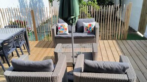 Eine Terrasse mit Korbmöbeln, darunter eine Couch und ein Tisch mit Stühlen.