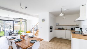 Eine moderne Küche mit weißen Schränken, einer Holz Arbeitsplatte und einem eingebauten Backofen. Es gibt einen Essbereich mit einem Holztisch und weißen Stühlen.