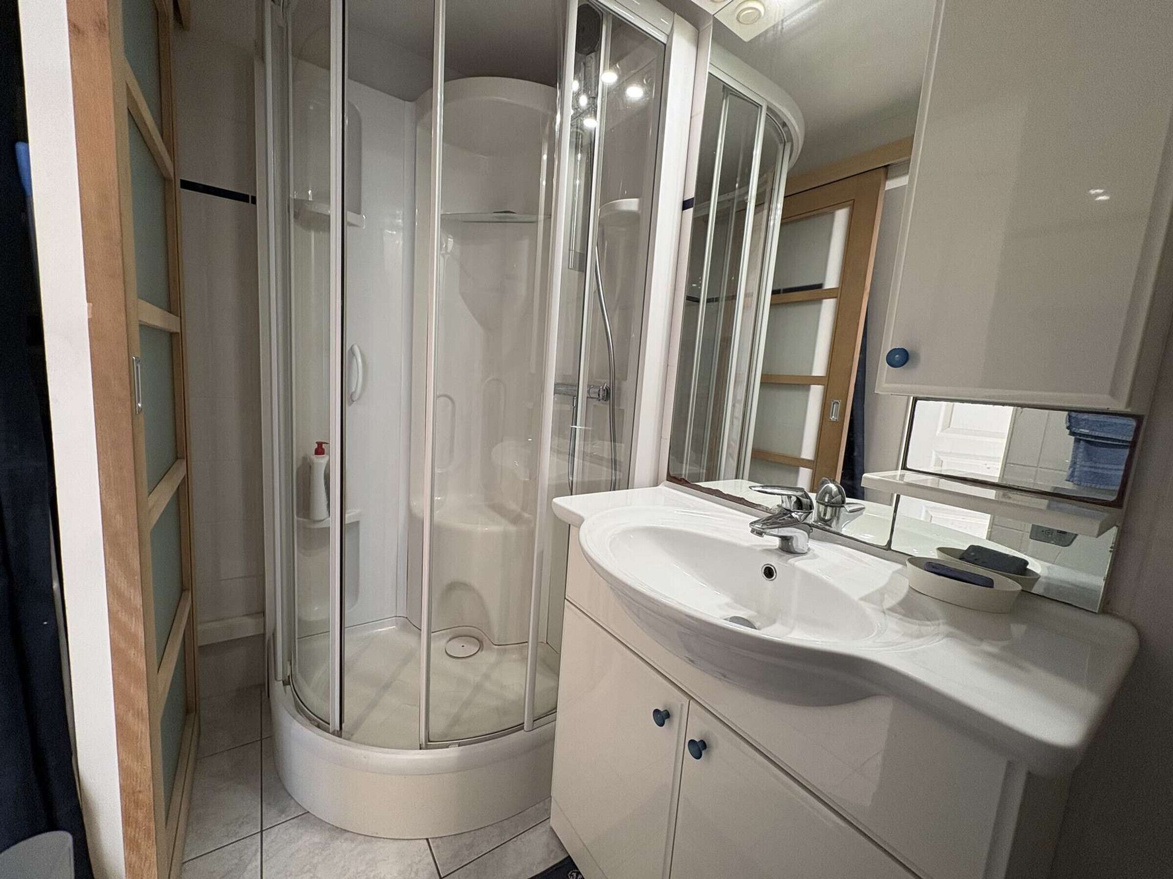 Un baño con cabina de ducha de vidrio, un lavabo blanco y un espejo.