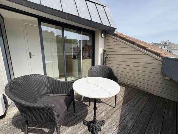 Ein Balkon mit Korbstühlen, einem Marmortisch, einer Schiebetür und Blick auf die Nachbarschaft.