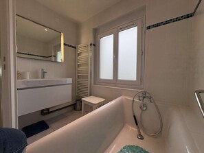 Ein Badezimmer mit Badewanne, Toilette, Waschbecken, Spiegel und Fenster.