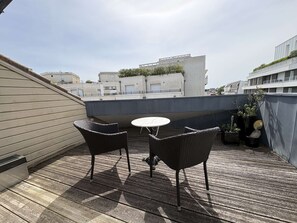 Una terrazza sul tetto con due poltrone in vimini e un tavolino rotondo, circondata da piante in vaso.