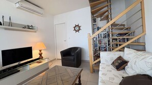 A living room with a flat-screen TV, a lamp, a sofa, a coffee table, a bookshelf, and a staircase. - Cozy 3-Level House in La Baule, 2 Terraces, Near Beach & Shops, Sleeps 6 (La Baule)