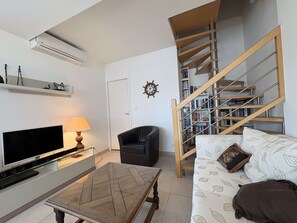 A living room with a flat-screen TV, a lamp, a sofa, a coffee table, a bookshelf, and a staircase.