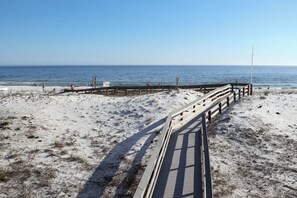 A beach with a wooden boardwalk leading to the water, a sandy shore, and a clear sky.