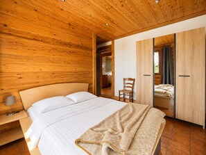 Een slaapkamer met een houten plafond, een bed met witte lakens, een stoel en een kledingkast.